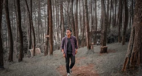 Full length of man standing amidst trees in forest