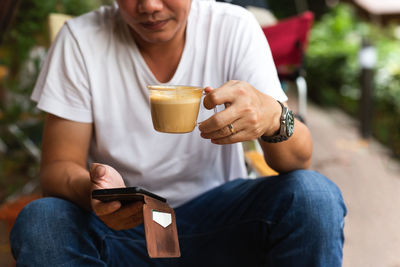 Man in jean and white t shirt drinking coffee and looking at cell phone in cafe outdoor.