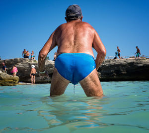 Rear view of shirtless man in sea against clear blue sky