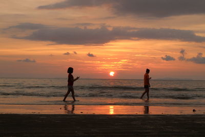 Silhouette people on beach against sky during sunset