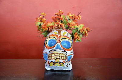 Skull with flowers on table against red wall