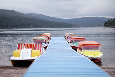 Boats moored pier at lake against sky