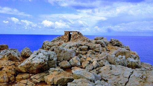 Rocks on cliff by sea against blue sky