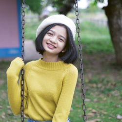 Portrait of smiling young woman on swing in playground