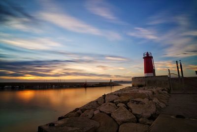 Lighthouse by building against sky during sunset