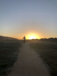 Rear view of man walking on field against sky during sunset