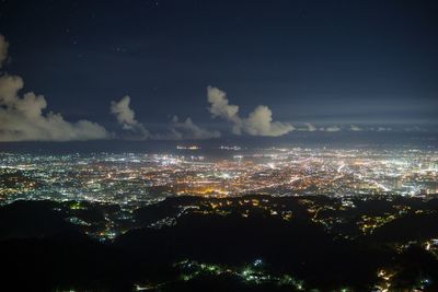 Illuminated city by sea against sky at night