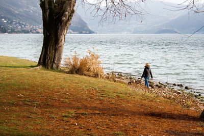 Rear view of woman walking with dog at lakeshore