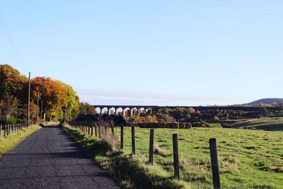 Road amidst field against clear sky