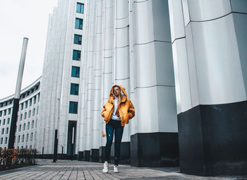 Woman wearing hood while standing by building in city