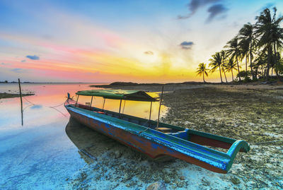 Boat moored on beach against sky during sunset