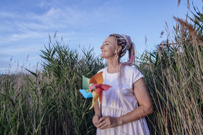 Girl with multicolored pigtails, face sideways, holding windmill in hands in summer, wind energy