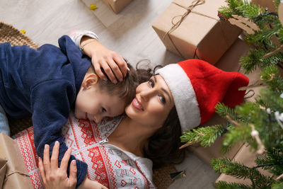 Top view mother and son in santa hats looking at camera and smiling while lying
