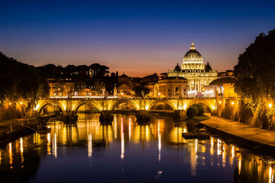 Illuminated bridge over river against st peter basilica at night