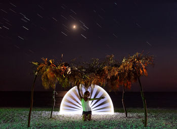 Woman kneeling with light painting at beach against sky