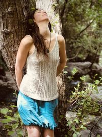Midsection of young woman standing by tree in forest