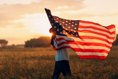 Low section of person standing on field against sky during sunset