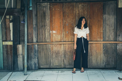 Full length of thoughtful woman standing against wooden wall