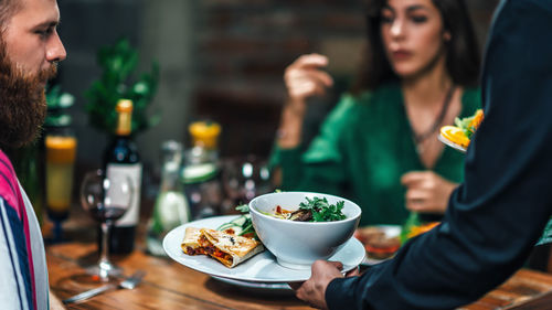 Cropped hand of waiter keeping food on table while young couple dating in restaurant