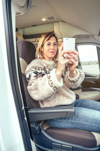 Woman taking picture with cell phone sitting in a camper van