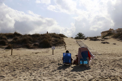 Hooded beach chairs on sand against sky