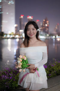 Portrait of young woman standing against illuminated christmas tree