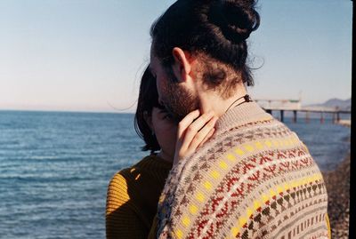 Young couple relaxing by sea against sky