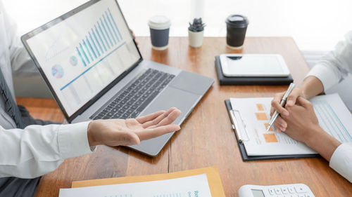 Midsection of colleagues with laptop analyzing charts on office desk