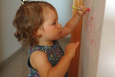 Side view of innocent girl drawing on wall at home