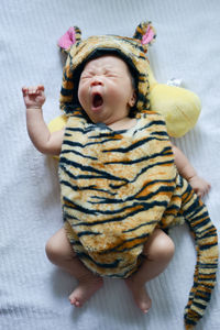 High angle view of baby in animal clothing yawning while lying on bed