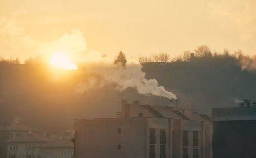 Smoke emitting from factory against sky during sunset