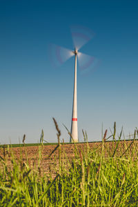 Wind turbine in motion on field against clear blue sky
