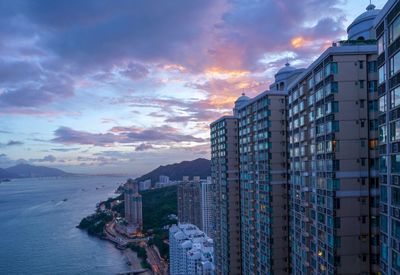 Modern buildings by sea against sky during sunset