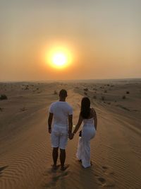 Rear view of women walking on sand during sunset