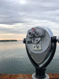 Close-up of coin-operated binoculars by river against sky