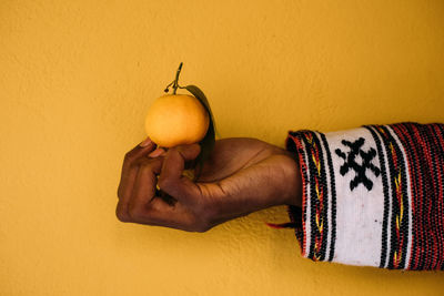 Close-up of man holding apple against orange background