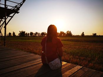 Rear view of man standing on field against sky during sunset