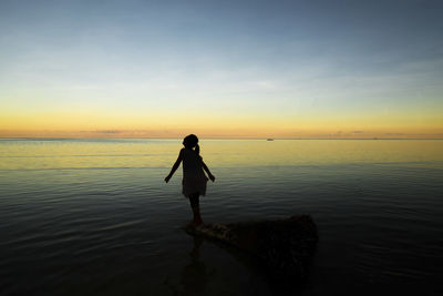 Silhouette man standing in sea against sky during sunset