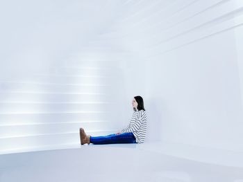 Side view of young woman sitting against wall