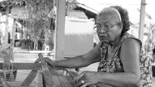 Senior woman weaving on loom while sitting outdoors