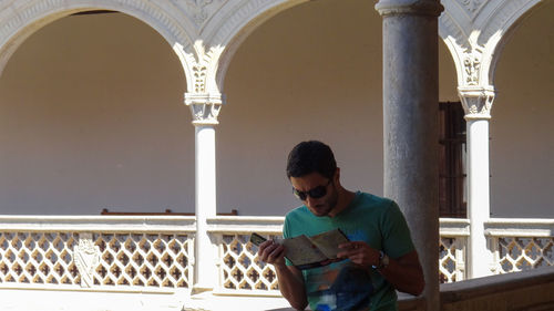 Young man looking away while standing against building