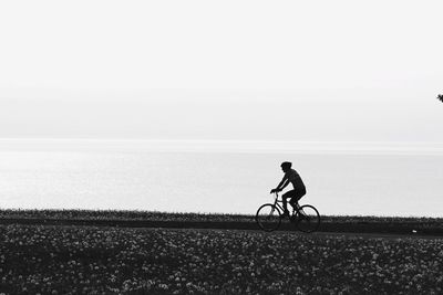 Man on bicycle by sea against clear sky