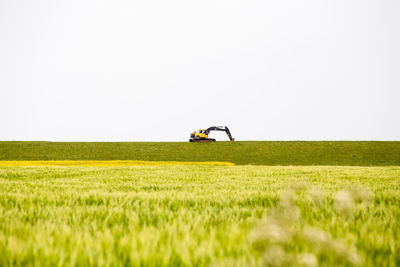 Excavator on grassy field against clear sky