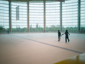 Full length of children ice skating against window