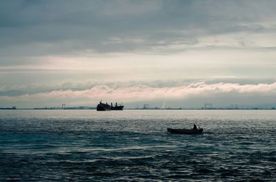 Boats sailing in sea against cloudy sky