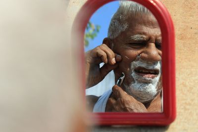 Reflection of senior man shaving beard seen in mirror