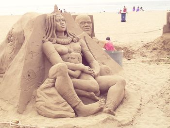 Statue on sand at beach against sky