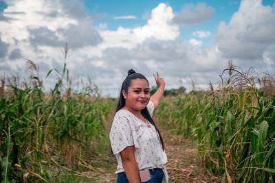 Smiling young woman standing on field against cloudy sky