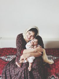 Portrait of smiling mother holding son while sitting on bed at home