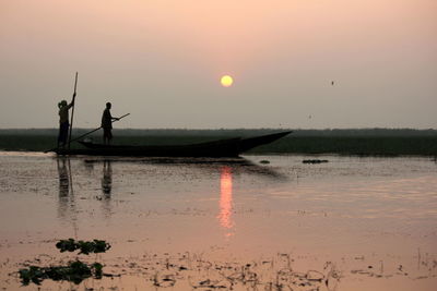 Men on boat at lake against sky during sunset